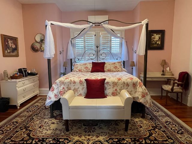 Room view of queen 4 poster bed, side table and antique desk